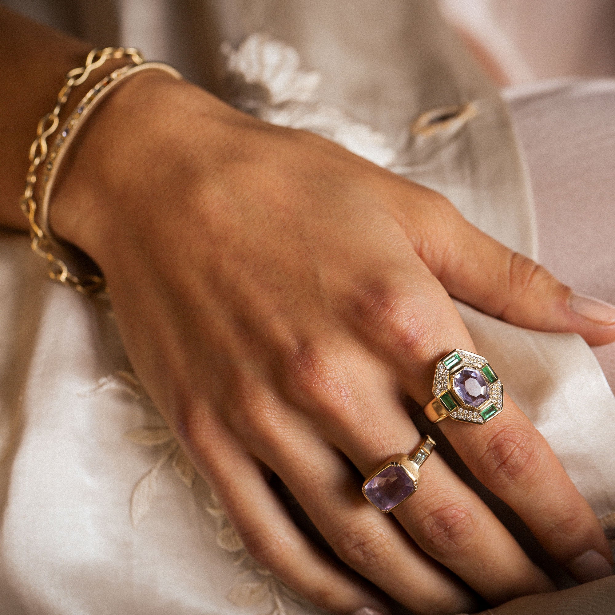 Hand wearing multiple rings with gemstones on a soft fabric background