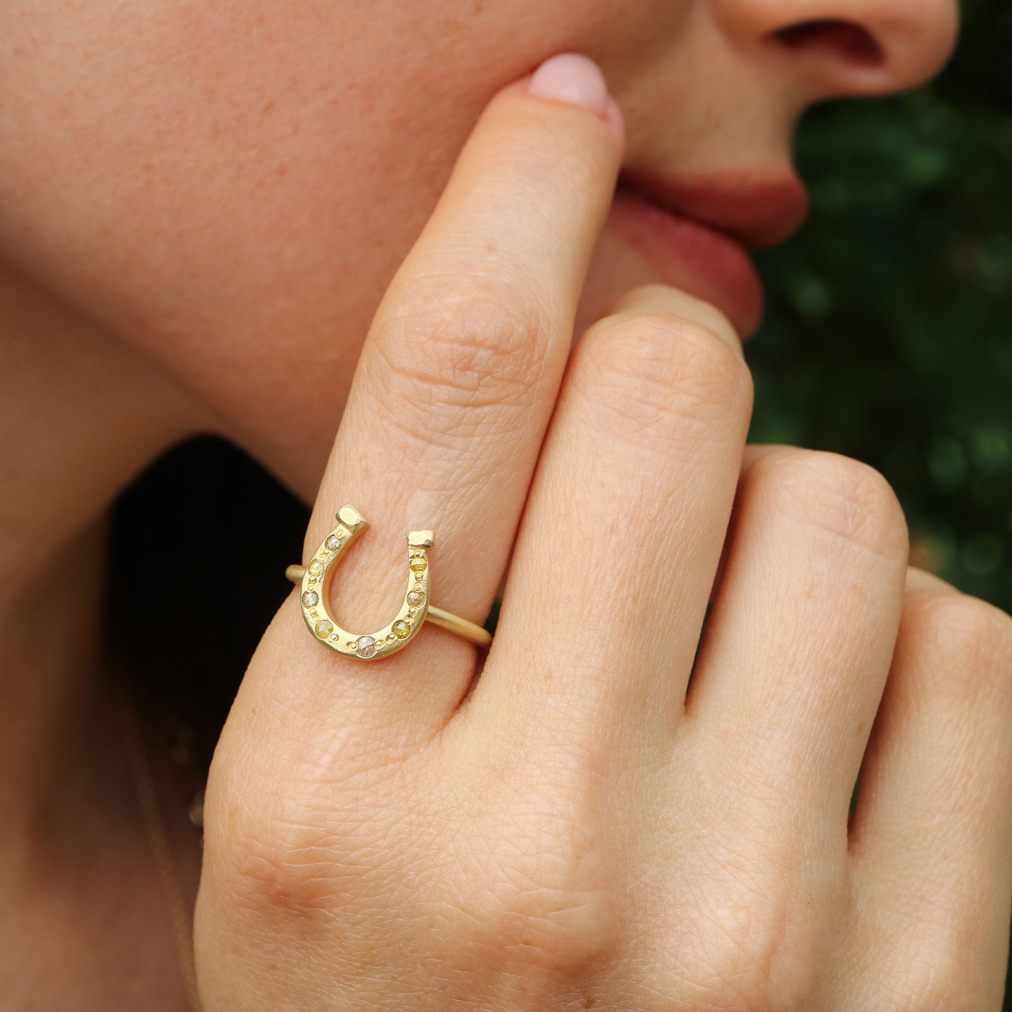 Gold horseshoe ring with embedded mixed rosecut diamond stones on a finger against a blurred background