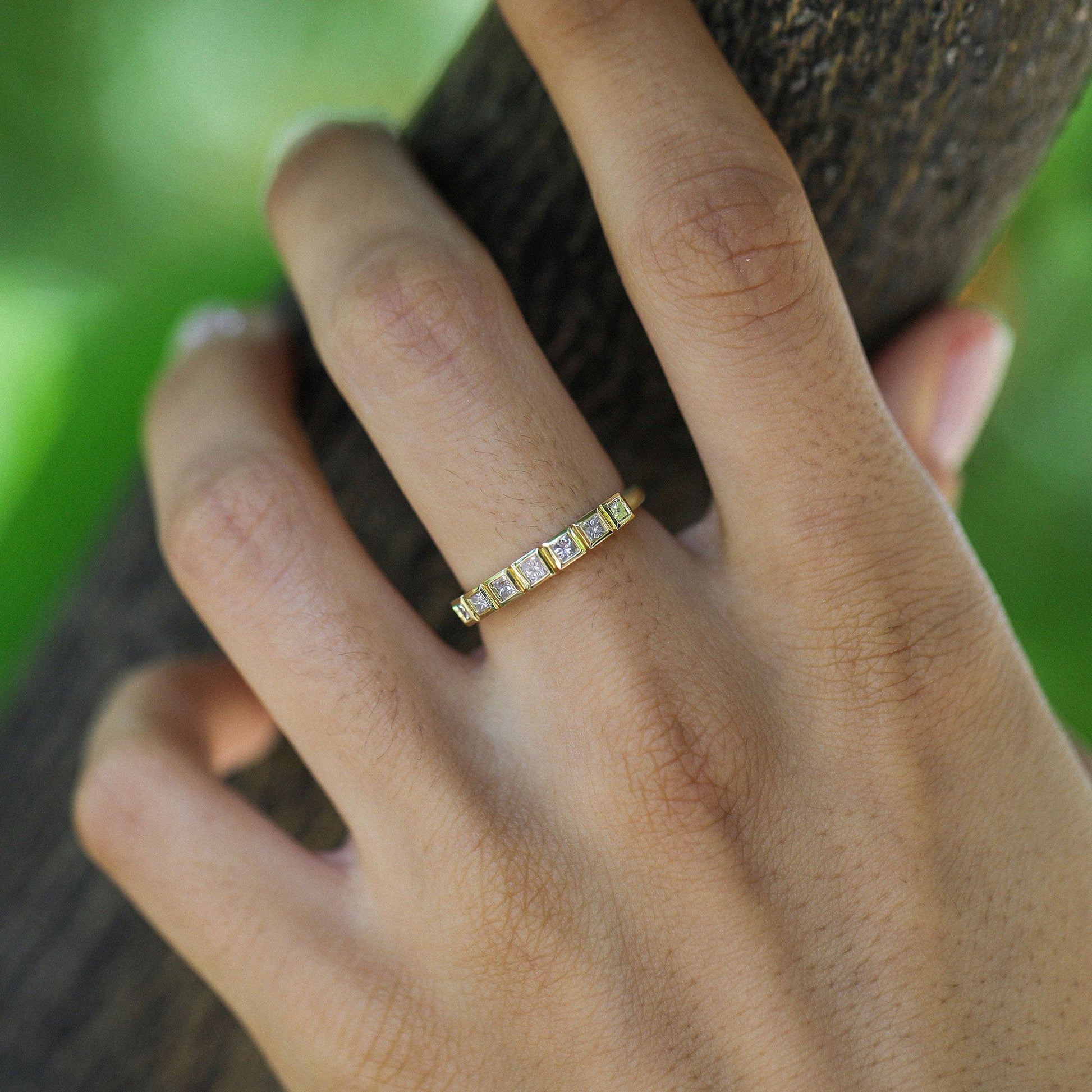close up of a hand wearing an 18k gold ring with pink princess cut diamonds designed by brooke gregson on a nature background