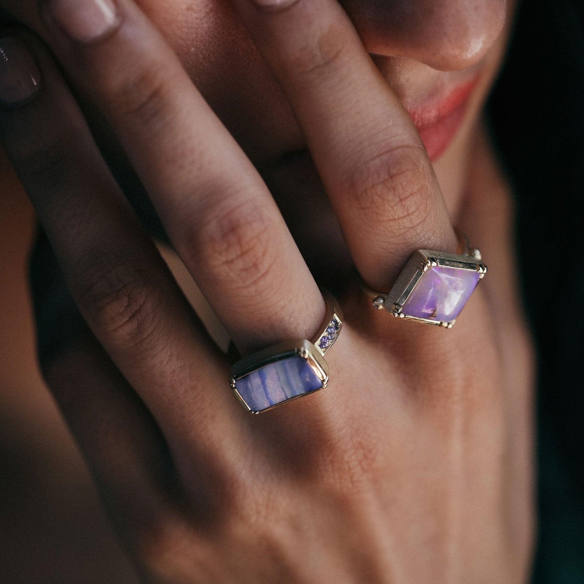 Close-up of a hand wearing two rings with purple gemstones on a blurred background