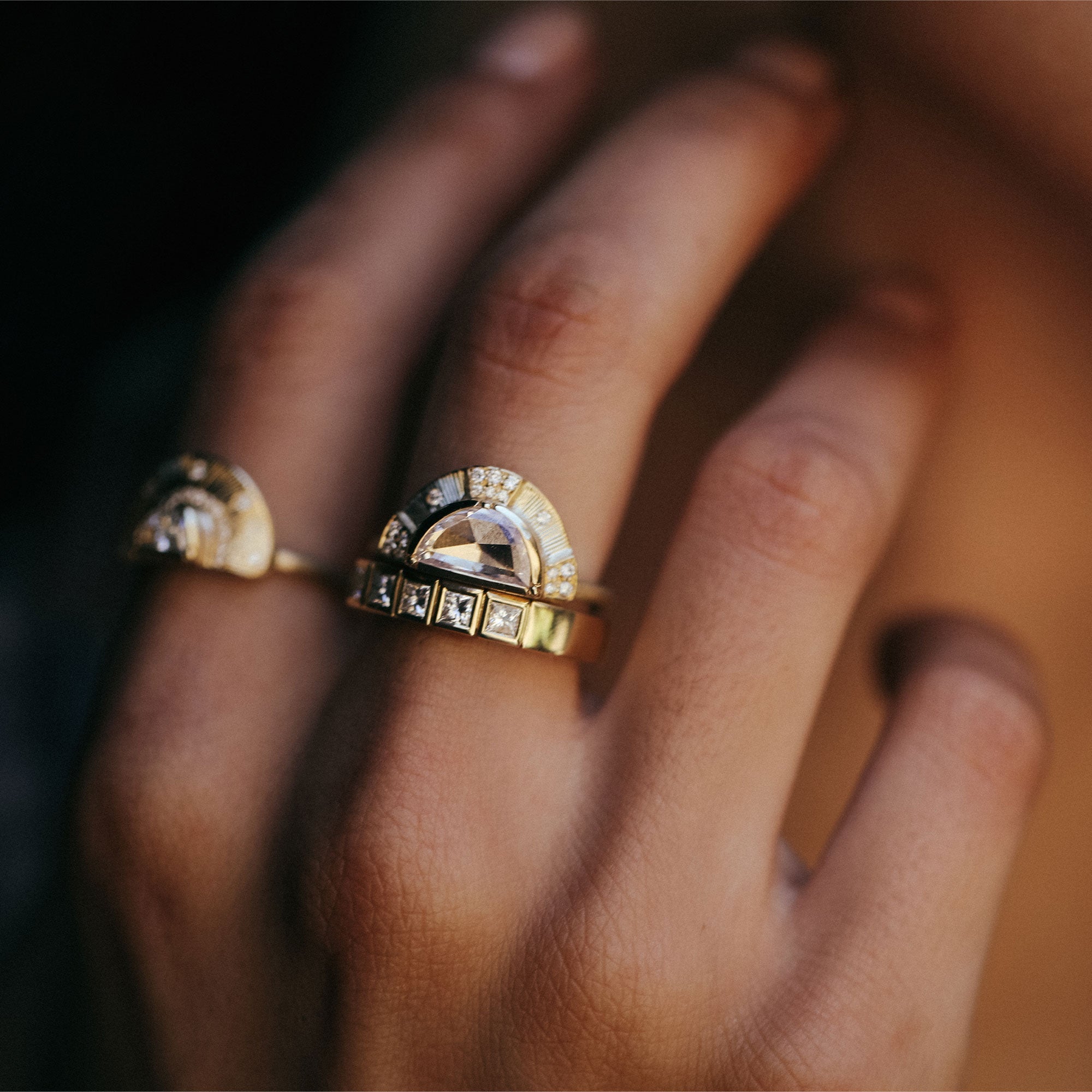 Close-up of a hand wearing two gold rings with gemstones on a blurred background