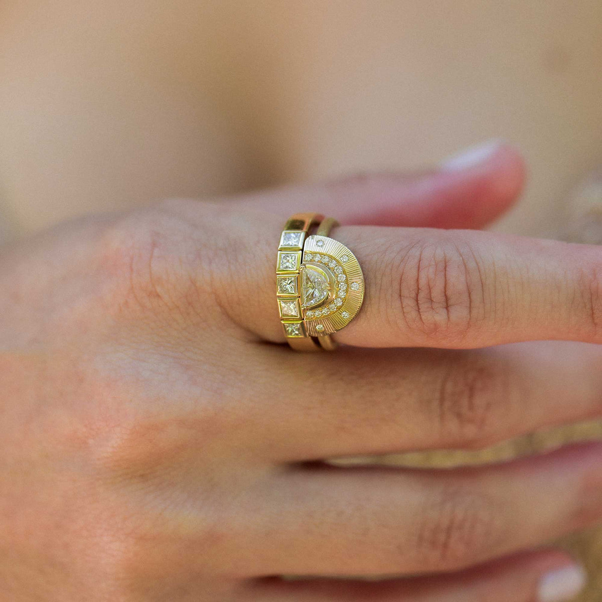 A close-up of a hand wearing a gold ring with a crescent moon hand engraved design and half moon diamond with accent white diamond pave. Worn alongside a gold eternity band with princess cut white diamonds. designed by brooke gregson handmade in london.