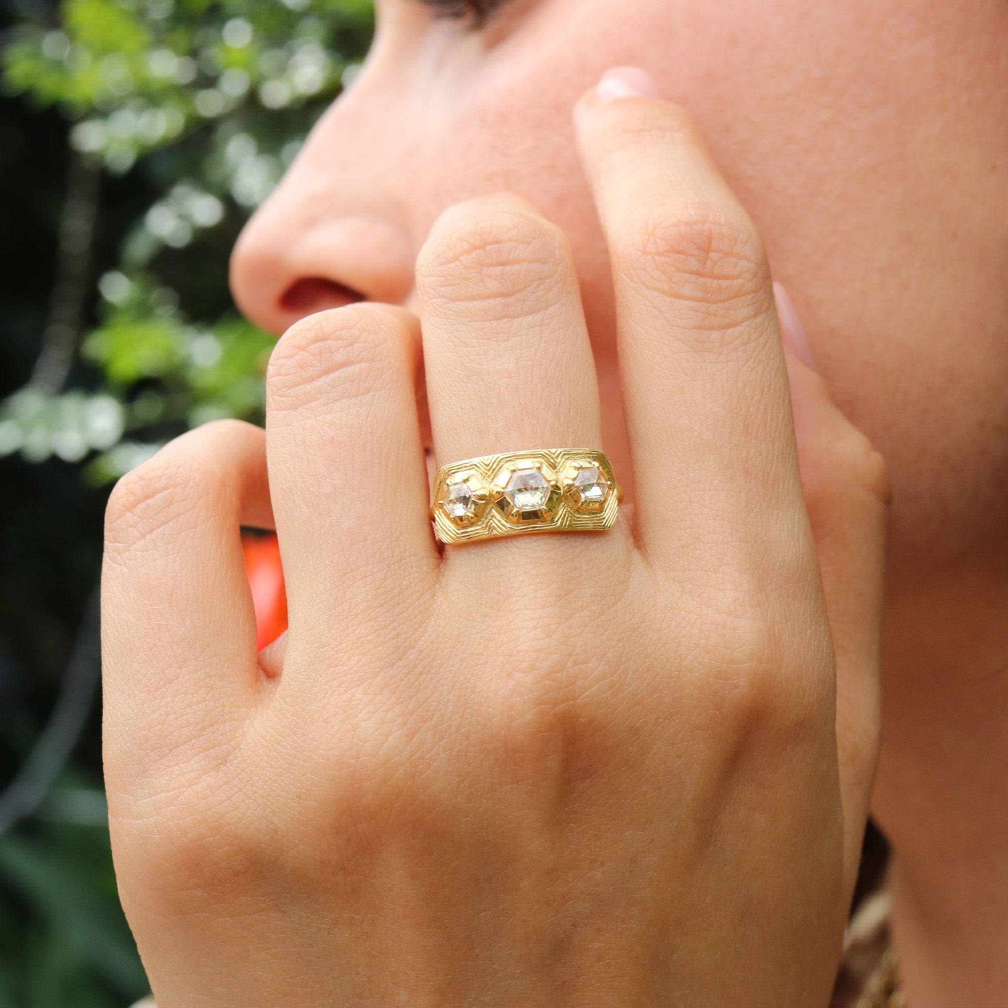 Hand wearing a 18k gold ring with hand engraving and three geo shape diamonds by Brooke Gregson Jewelry.