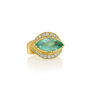 A gold ring featuring a marquise-cut green emerald gemstone surrounded by a halo of small diamond stones, set against a clean white background with a soft reflection.