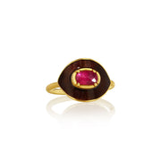 A gold ring featuring a large, scalloped dark reddish-brown enamel inlay and a central oval pink ruby gemstone, shown on a clean white background with a soft reflection.