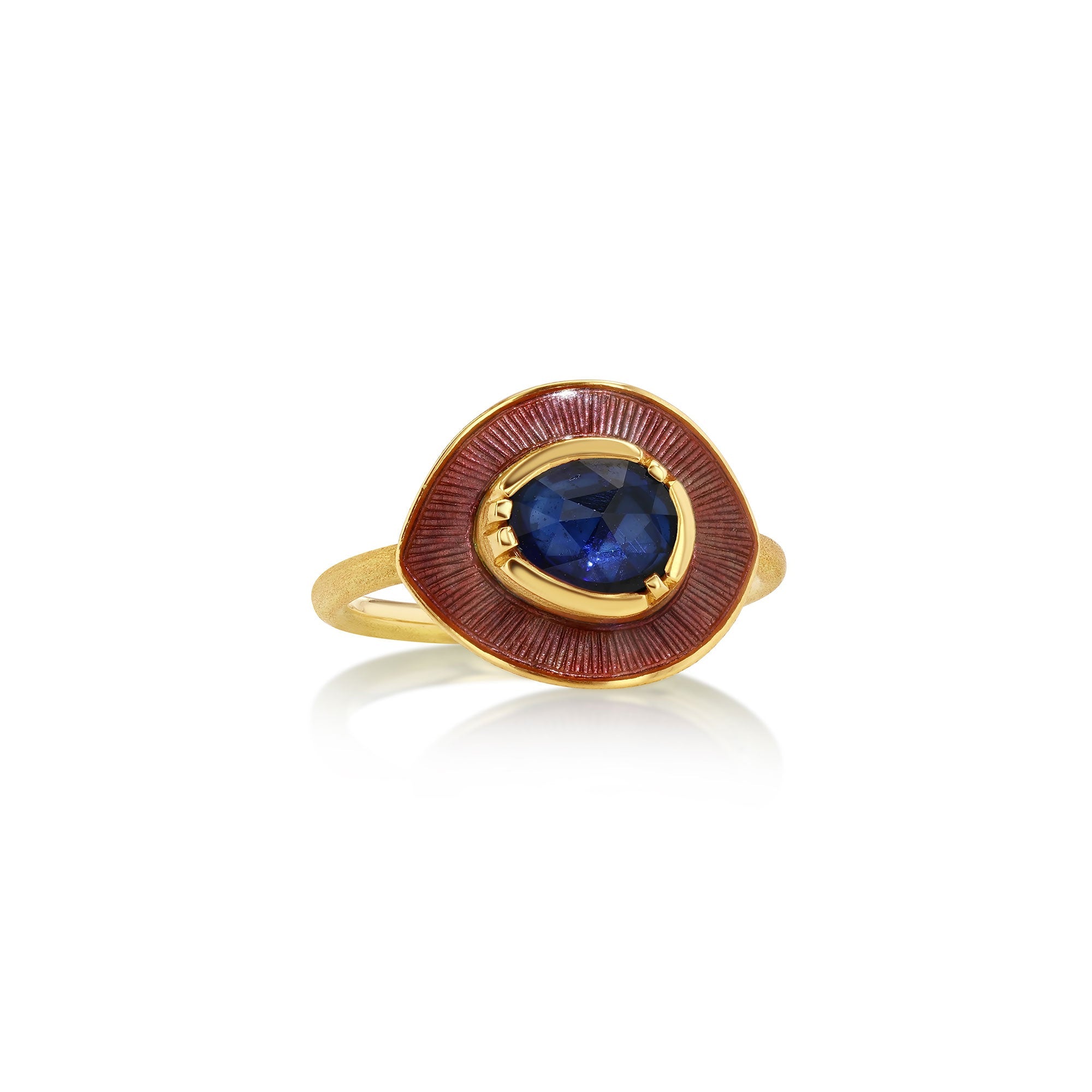 A gold ring featuring a central oval blue sapphire gemstone surrounded by a textured, reddish-brown circular enamel setting, all on a polished gold band, set against a clean white background with a soft reflection.