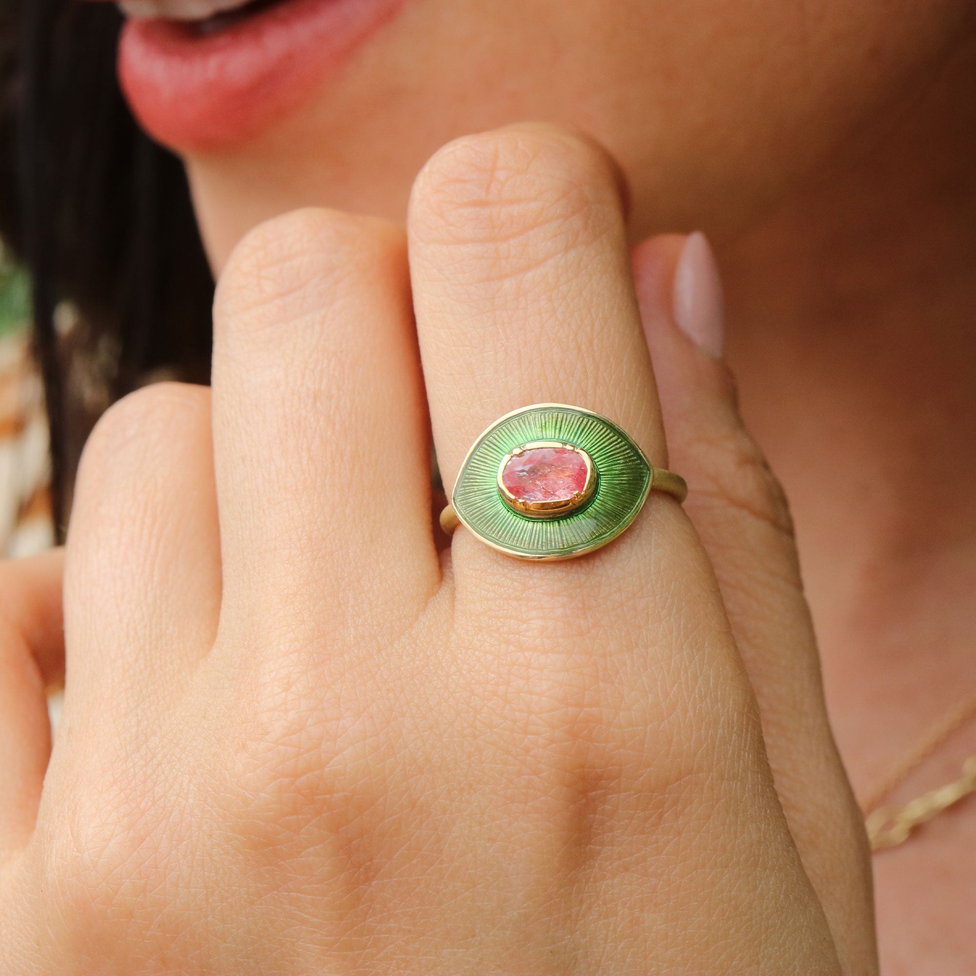 Close-up of a hand wearing a green enameled ring with a pink sapphire gemstone.