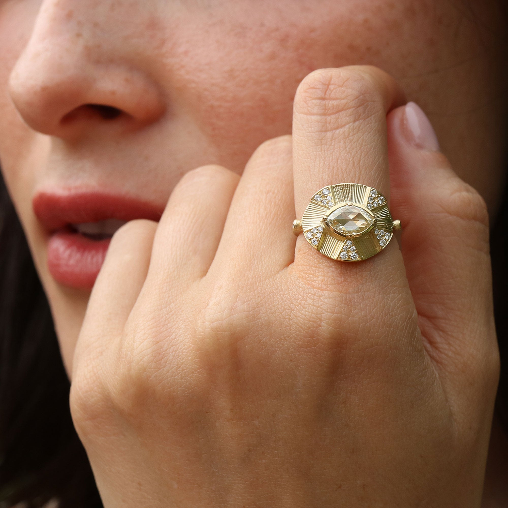 Close-up of a hand wearing a gold hand engraved ring with diamond gemstones, held near the face.