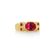 A yellow gold hand engraved ring featuring a large oval-cut pinkish-red tourmaline central gemstone, flanked by smaller square pink sapphire gemstones on the shoulders, set against a plain white background.