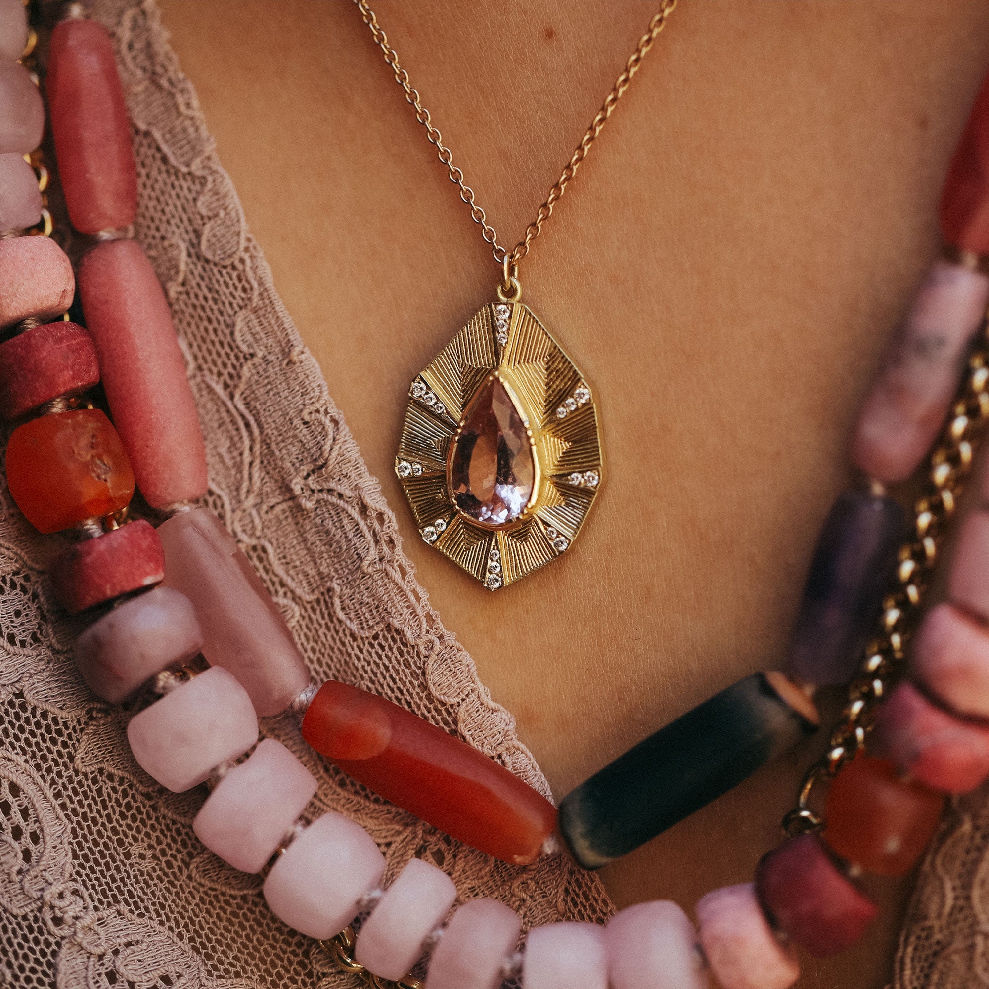 Gold necklace with a teardrop pendant worn by a person on a lace fabric background