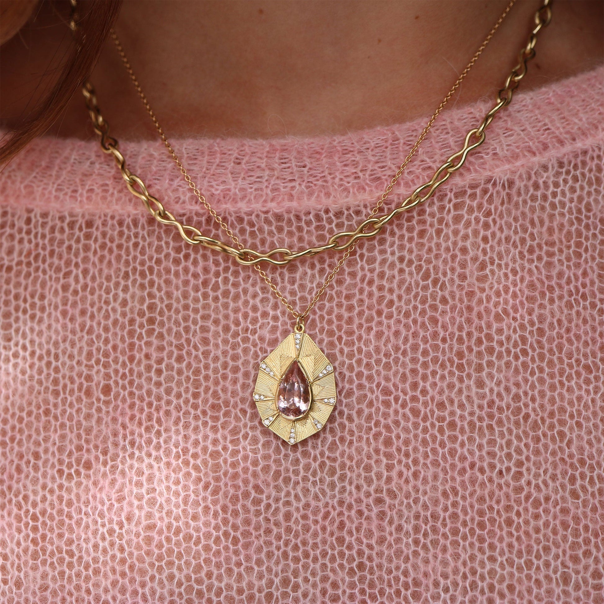 Gold necklace with a teardrop pendant on a pink textured fabric background