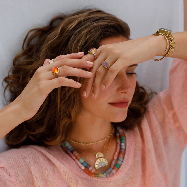 Woman wearing multiple rings and a pink sweater with a neutral background